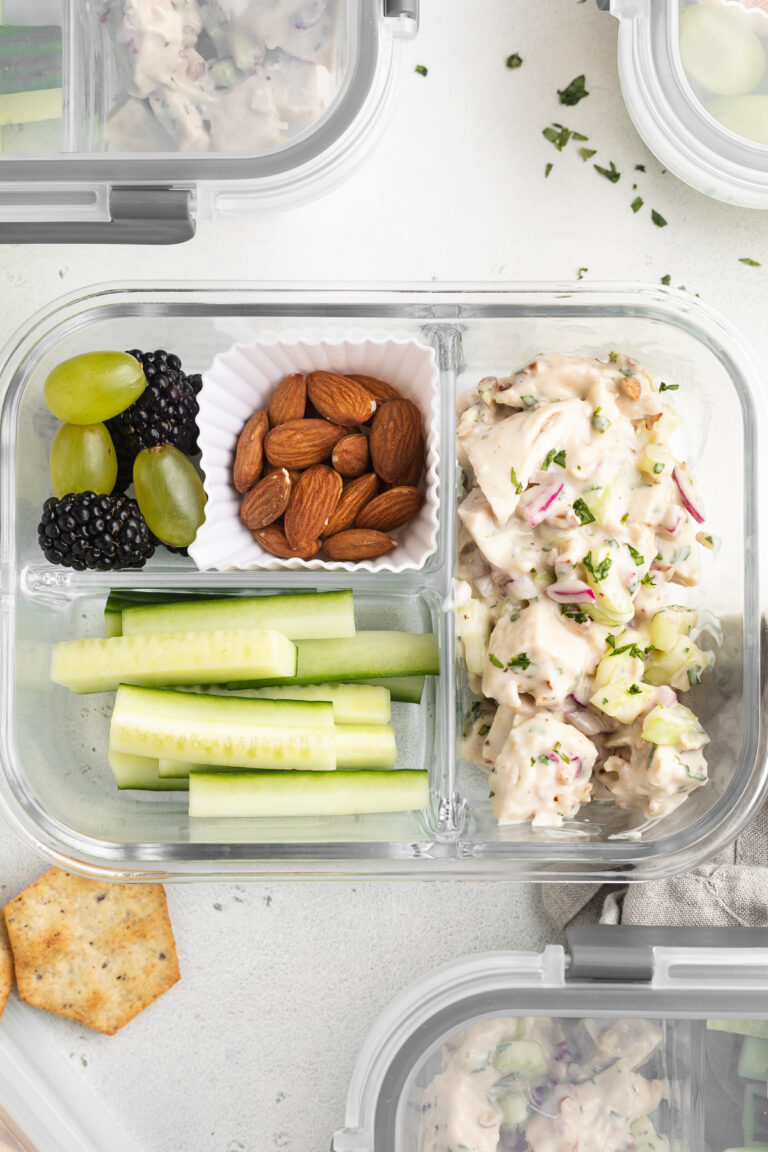 overhead image of chicken salad lunch boxes with cucumbers, almond, grapes, and blackberries