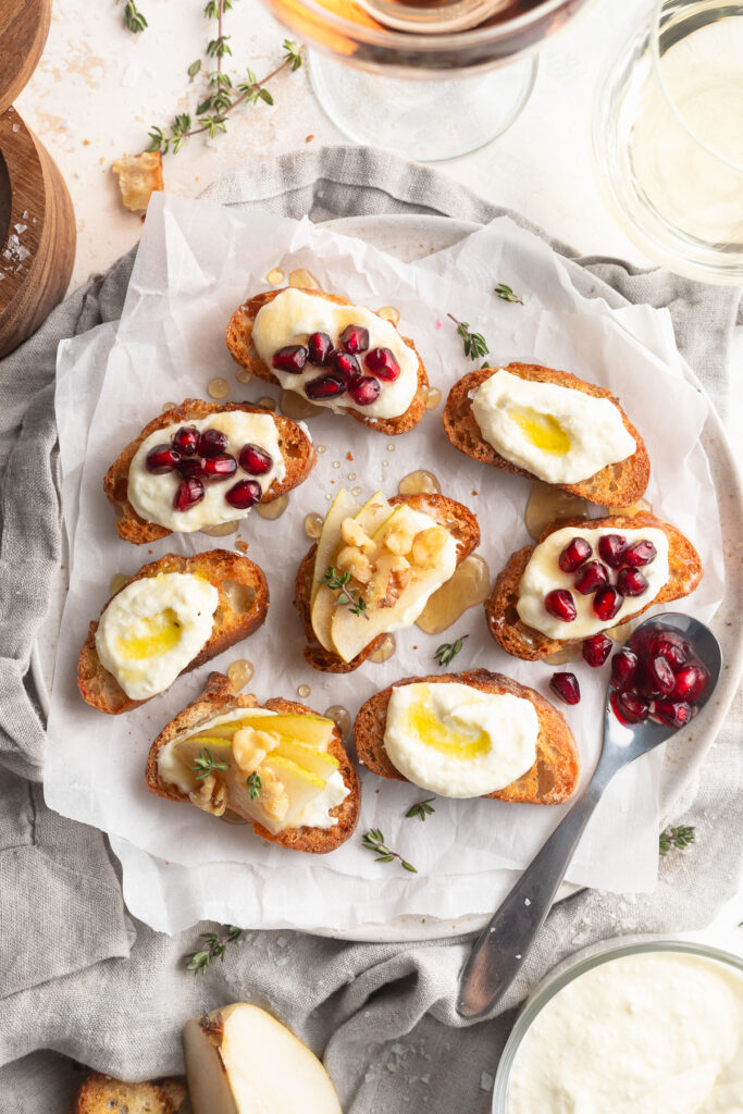whipped feta crostini 3 ways on a plate with wine and fresh thyme on the side.
