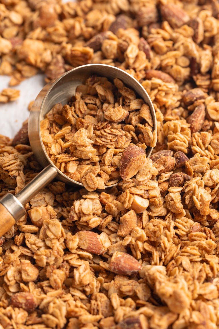 Homemade granola being scooped off a baking sheet with a measuring scoop.