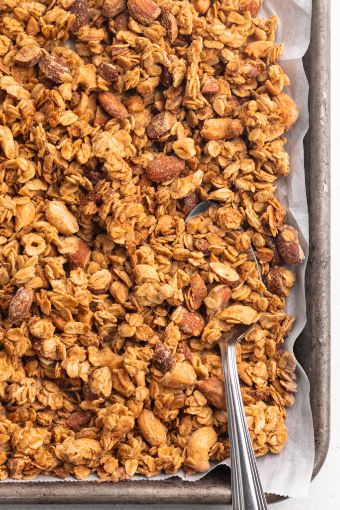 Homemade granola on a baking sheet with a serving spoon.