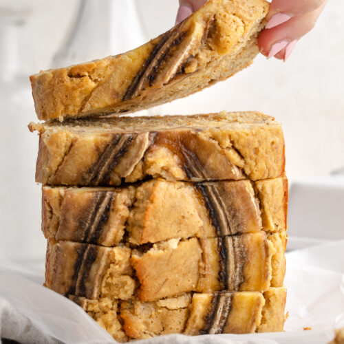 Stacked slices of 4 ingredient banana bread, with a hand lifting the top slice.