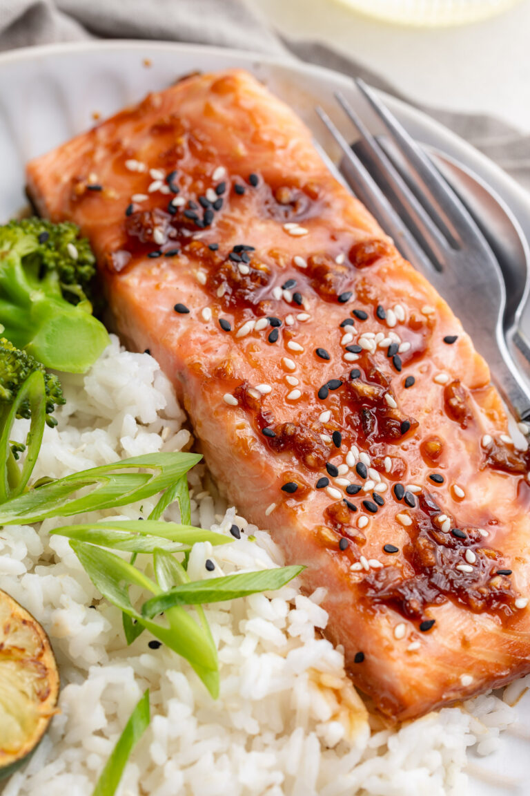 Close up image of a honey teriyaki salmon fillet on a plate with rice and sliced green onion.