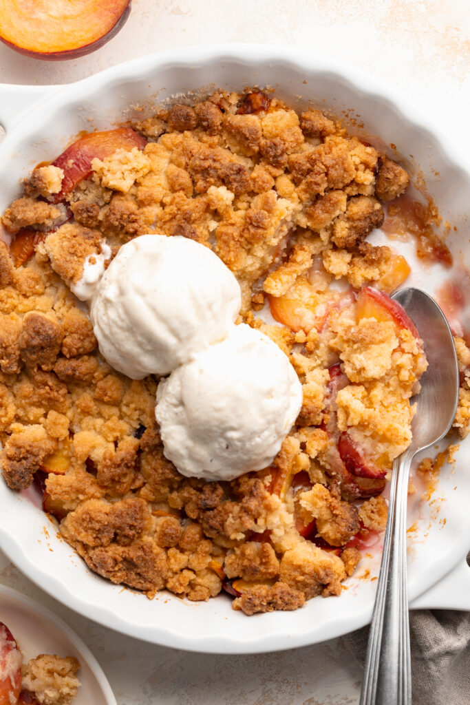 overhead image of 4 ingredient peach cobbler in a baking dish with ice cream on top.