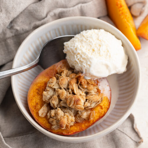 single serve peach crisp dessert in a bowl with a scoop of vanilla ice cream.