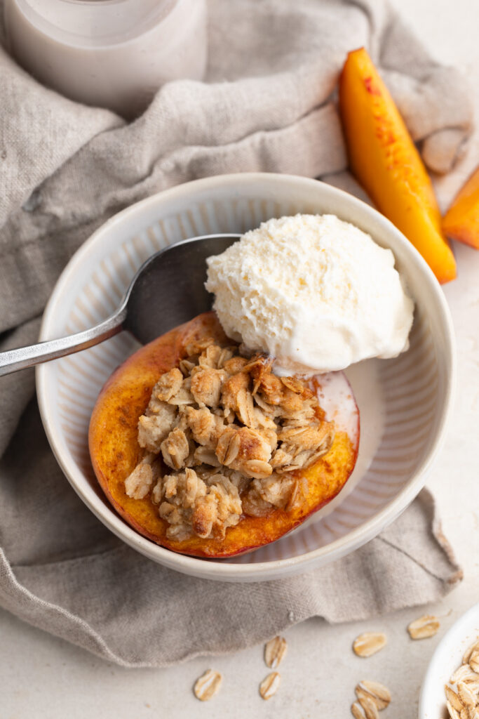 single serve peach crisp dessert in a bowl with a scoop of vanilla ice cream.
