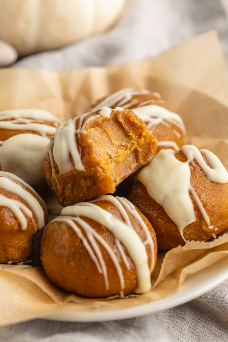 pumpkin protein balls on a plate with white chocolate drizzled on top.