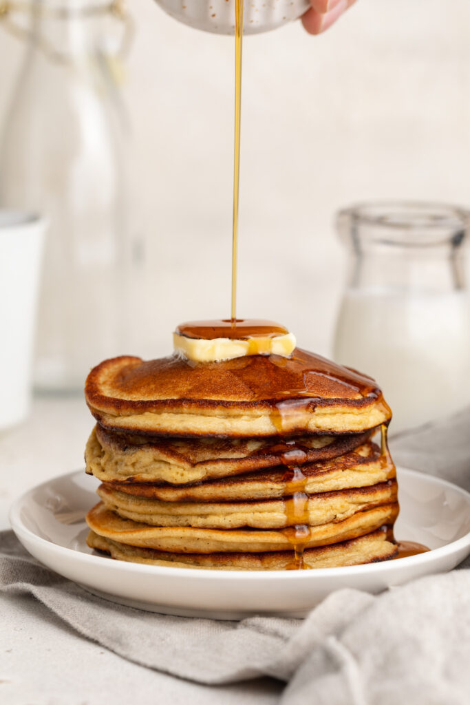 maple syrup being poured over a stack of pancakes.