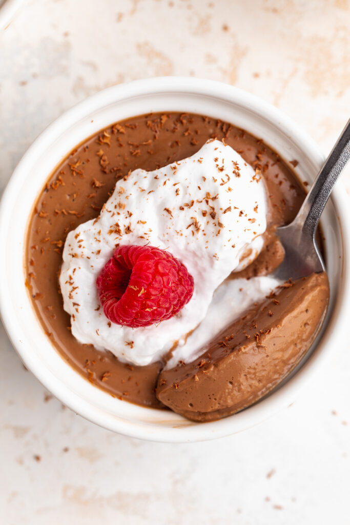 Close up image of silken tofu chocolate mousse in a small ramekin with whipped cream and a raspberry on top.
