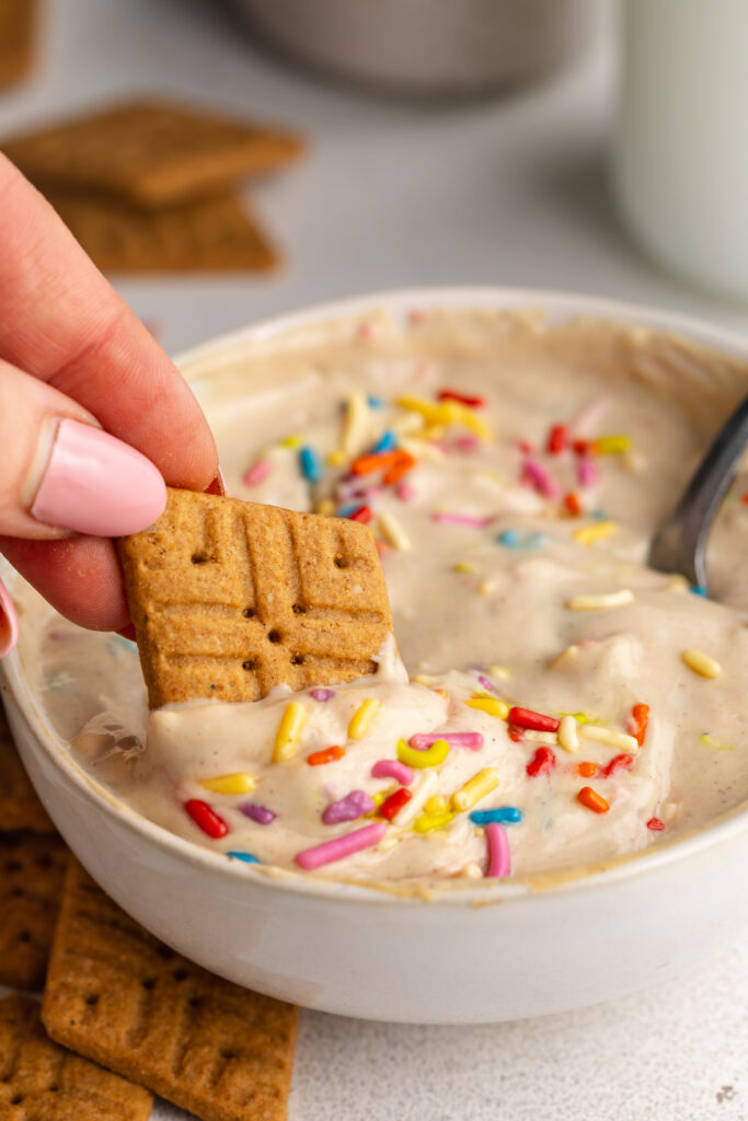 a gluten-free cookie being dipped into 4 ingredient protein dunkaroo dip in a bowl.