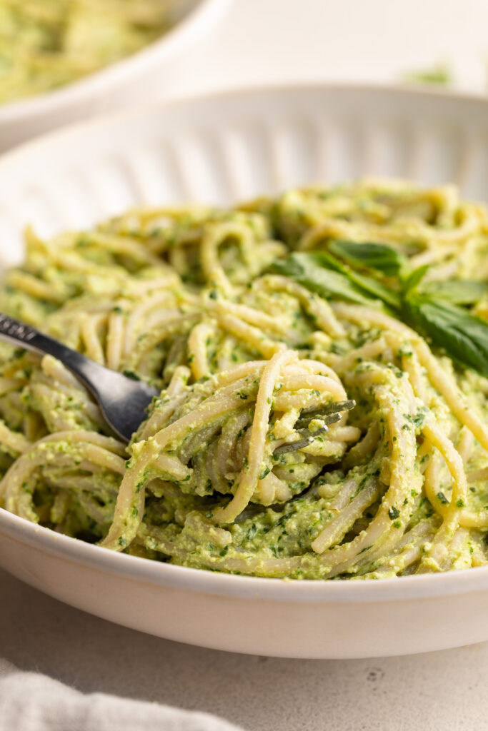 close up image of high protein pesto pasta twirled around a fork.