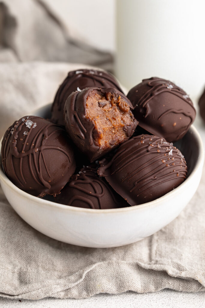 healthy no-bake brownie balls in a small bow, one with a bite taken out.