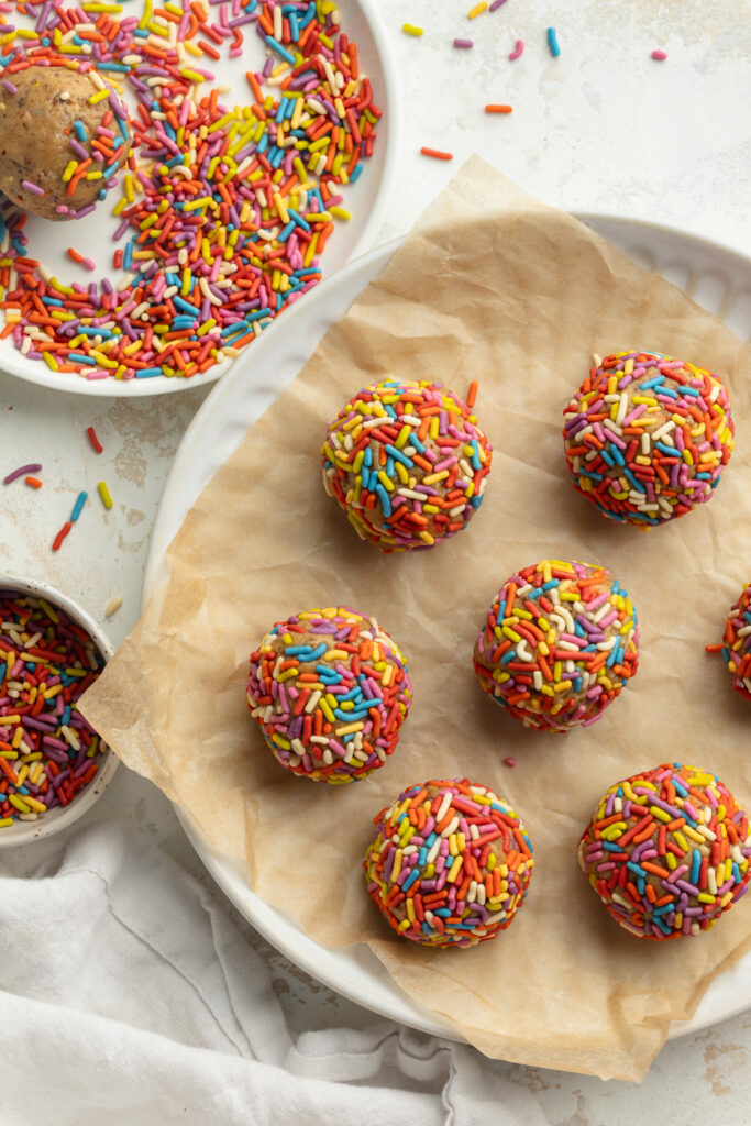 overhead image of birthday cake energy bites being rolled in sprinkles.