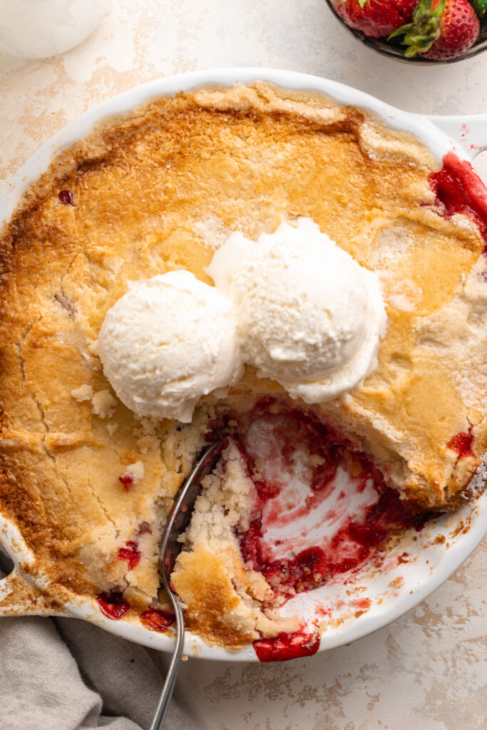 overhead image of 3 ingredient strawberry dump cake in a baking dish with ice cream on top.